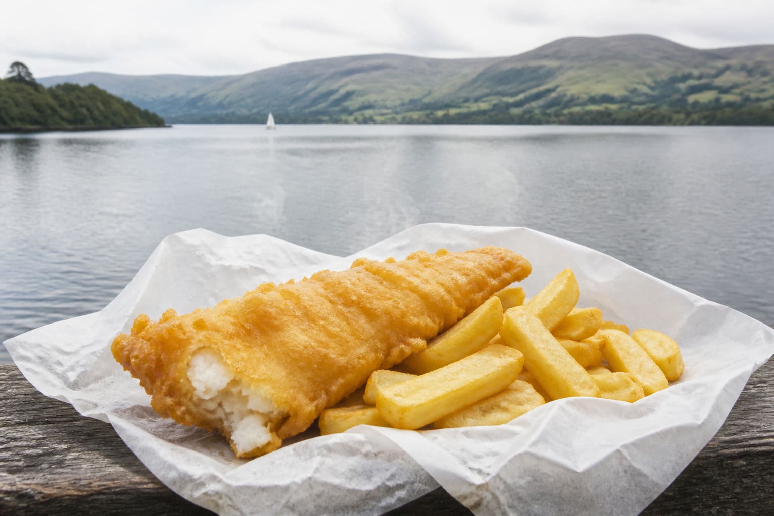 Freshly fried fish and chips in paper on a bench beside Lake Windermere